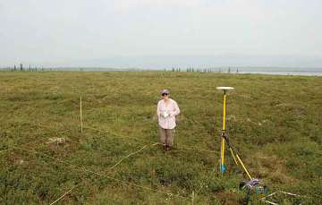 woman stands near ground plots and soil monitoring equipment in the open tundra