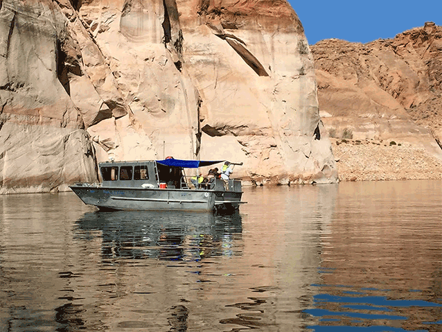 Silver boat on calm water in front of a tall cliff