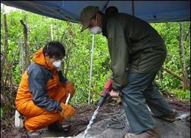 two researchers drill into bedrock to install GPS unit