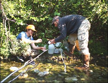 two scientists collect water from a stream