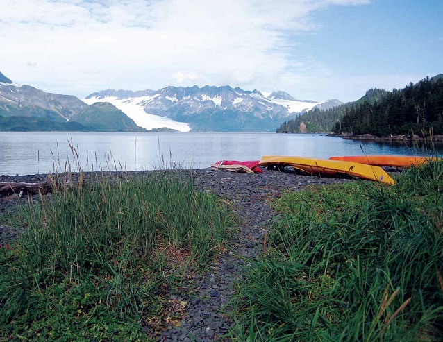 two kayaks sit on a beach with glaciers and mountains in the background