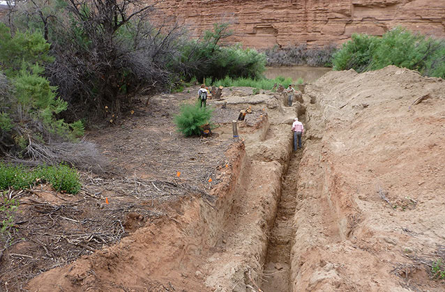 a narrow trench in the earth with people walking in it