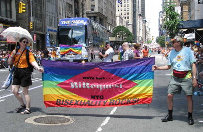 A march down a street with two people holding a rainbow banner A march down a street with two people holding a rainbow banner