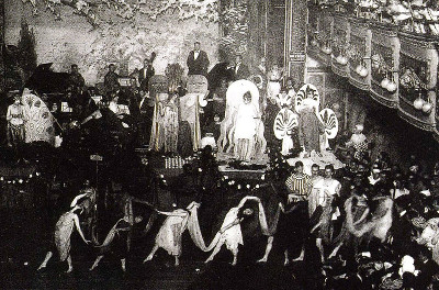A line of dancers in costumes in front of a stage with a band and performers A line of dancers in costumes in front of a stage with a band and performers