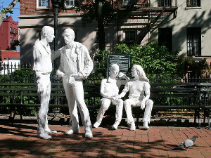 White statues of people in a park, two standing and two sitting on a park bench White statues of people in a park, two standing and two sitting on a park bench