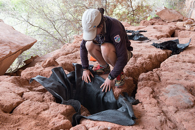 a woman places black cloth into an earthen hole