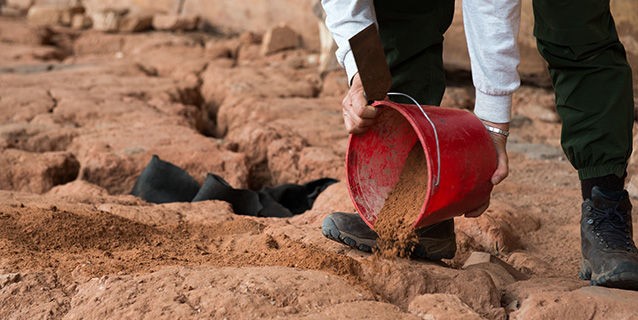 two hands pour soil from a red bucket