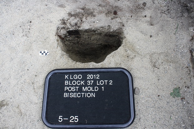 Sandy soil with dark half-circle depression and black and white sign