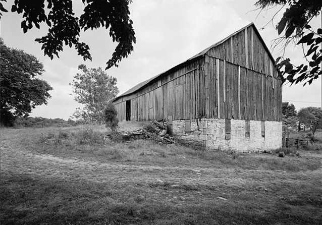 A large wooden barn with a stone foundation on sloping terrain