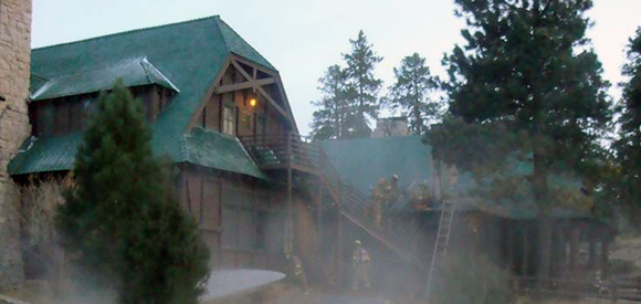 Exterior lodge during fire with evergreen trees nearby.