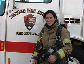 Woman poses next to fire engine in firefighting gear