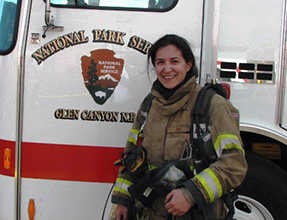 Woman poses next to fire engine in firefighting gear Woman poses next to fire engine in firefighting gear