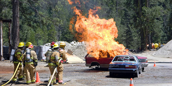 Firefighters putting out a large car fire during a training exercise.