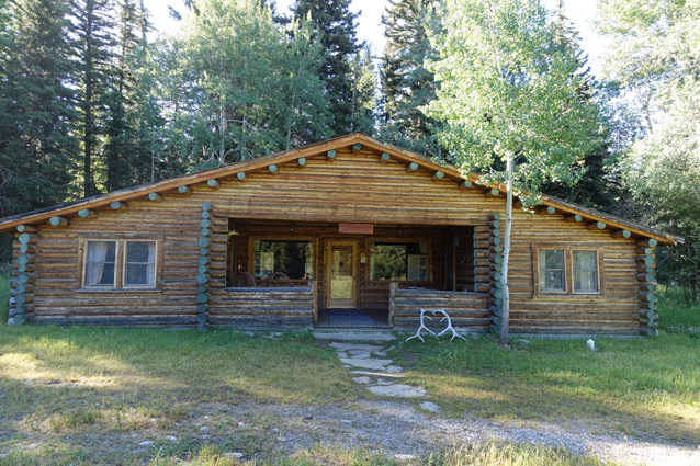 A square log cabin has a sloping roof and sheltered front porch. A square log cabin has a sloping roof and sheltered front porch.