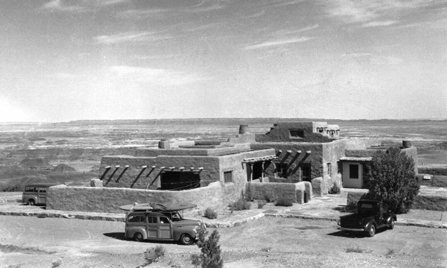 Several 1940s vehicles in the parking area in front of a low adobe structure