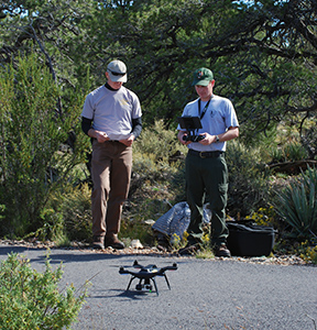 A drone sits on an asphalt path while two men stand nearby.