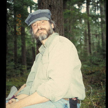 A smiling man with a beard and a cap, his body turned to the side but head facing the camera