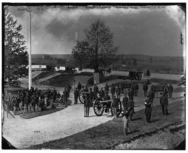 Historic image showing uniformed soldiers gathered around cannons and fortifications 