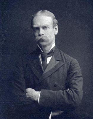 Historic image of man in suit and tie, arms crossed, with a long mustache