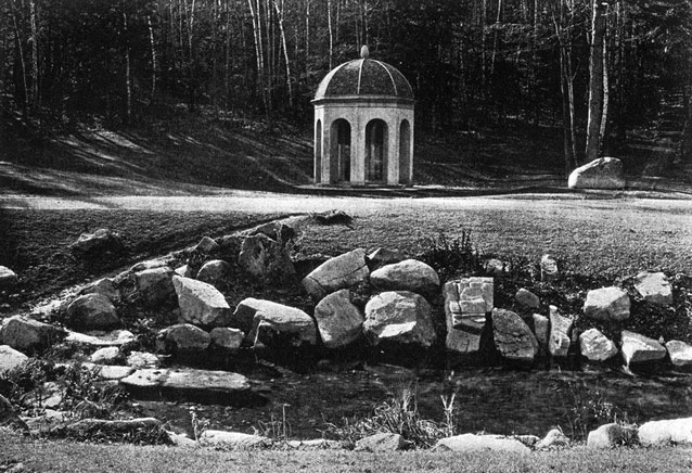 Large stones line a pool of water in the foreground, with a round domed structure in the rear. 