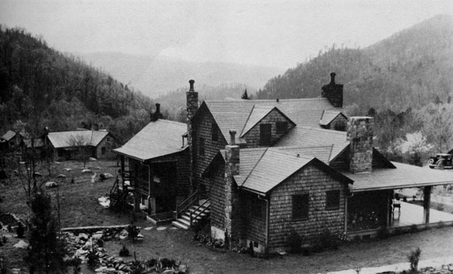A large, rustic house in a mountain setting with several stone chimneys 