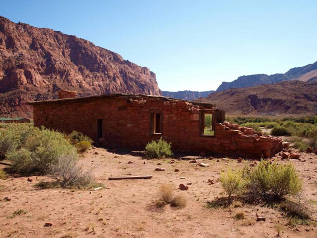 A single story stone structure, the roof partially gone, framed by red cliffs in a dry environment