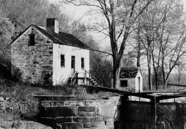 Historic image show two rectangular stone structures along the side of a stone-lined canal. Historic image show two rectangular stone structures along the side of a stone-lined canal.