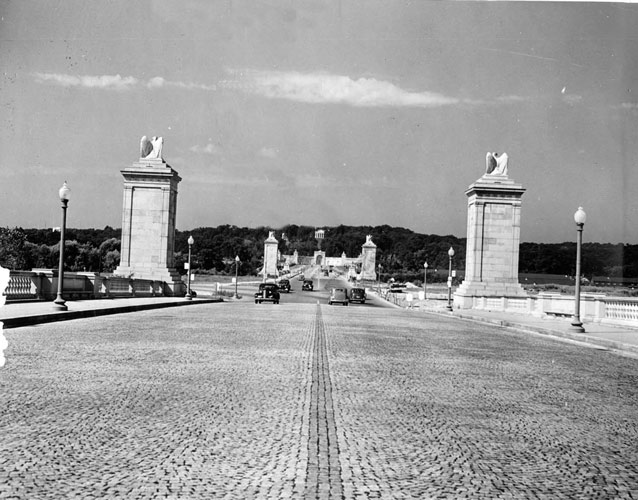 Eagle sculptures mount the tops of wide stone columns alongside a textured road surface.