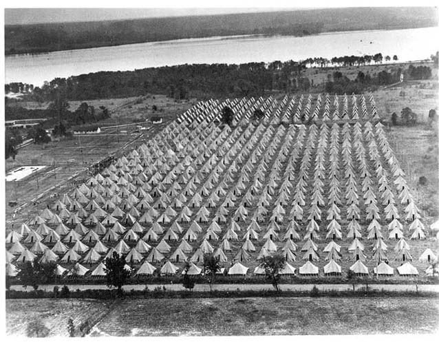 Symmetrical row of tents on a flat, open field beside the Potomac River