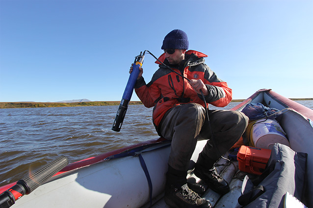 person sitting in the back of a raft using a scientific instrument in the water