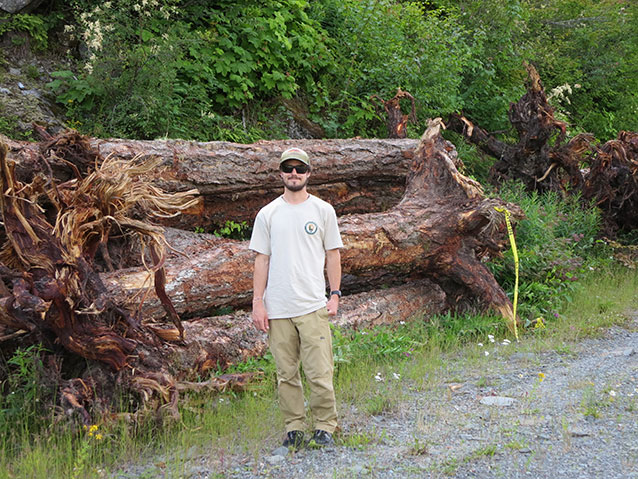 Intern standing by log pile