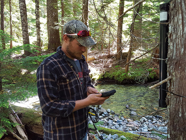 Intern with hand held gps standing near stream Intern with hand held gps standing near stream