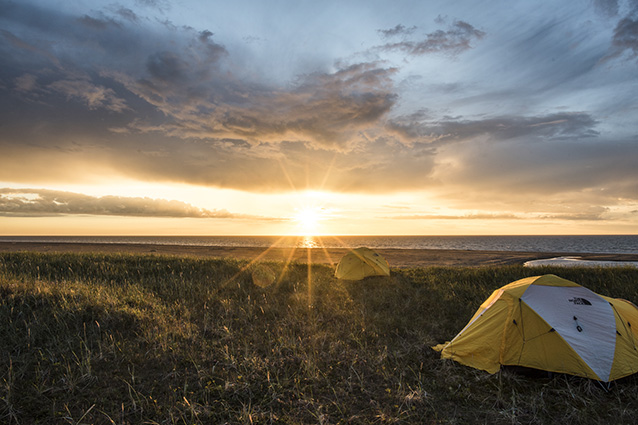 sun setting behind a tree-less landscape, with a yellow tent in the foreground