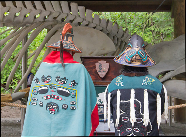 two people in traditional alaska native outfits standing near a whale skeleton two people in traditional alaska native outfits standing near a whale skeleton