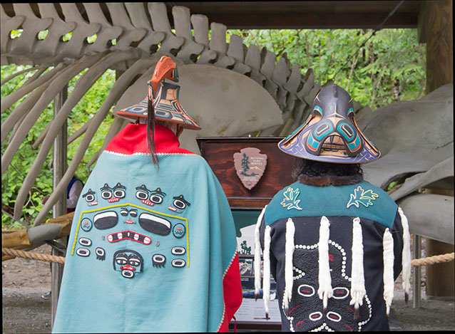 two people in traditional alaska native outfits standing near a whale skeleton