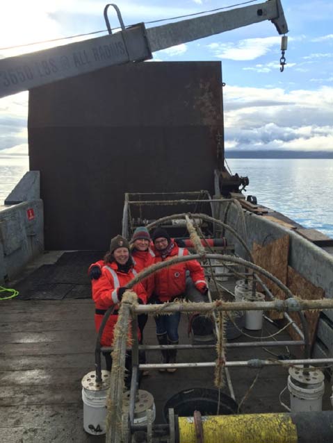 three people in safety orange suits standing on a ship