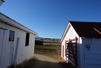 A view between two low buildings is open pastureland and distant mountains