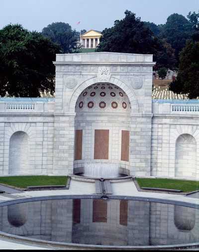 Round pool of water in front of a curving stone memorial, with a rectangular form and half dome