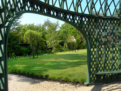 A green lawn extends beyond the framework of an arching green pergola. A green lawn extends beyond the framework of an arching green pergola.