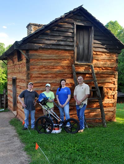 Two men and two women with survey equipment in front of a log cabin