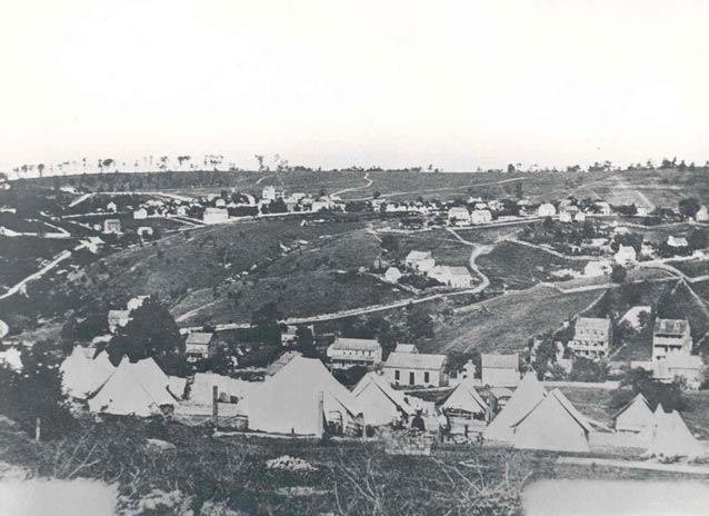Historic photo of tent camp, with rolling rural landscape dotted with houses beyond. Historic photo of tent camp, with rolling rural landscape dotted with houses beyond.