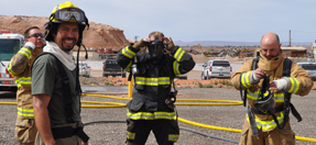 A firefighter looks at the camera while other firefighters put on full protective gear