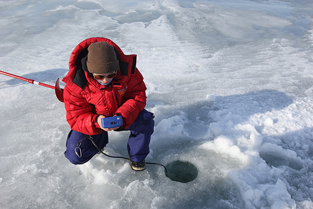 woman in red parka kneeling by a hole in ice woman in red parka kneeling by a hole in ice