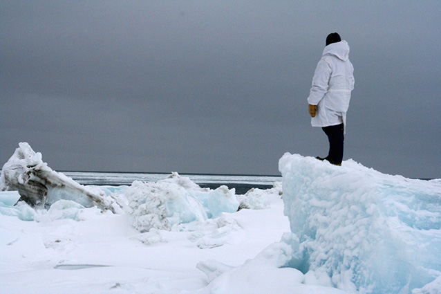 man in a white parka standing on large block of ice looking toward the ocean man in a white parka standing on large block of ice looking toward the ocean