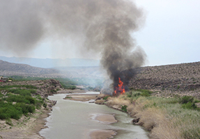 River, large flames on riverbank, and small nearby community.