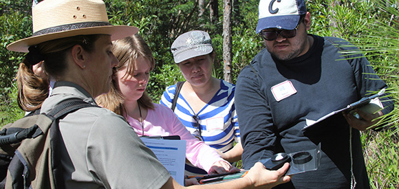A ranger holds a scientific instrument while several teachers look on. A ranger holds a scientific instrument while several teachers look on.