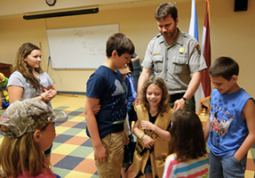 A ranger places a vest with 45 pounds of weight in it on the shoulders of a young girl.