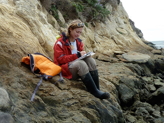 intern on coastal bluff writing in field notebook