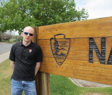 NPS Employee Charles Notzon standing next to a wooden NPS sign