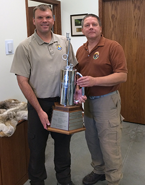 Two men stand with drip torch award.
